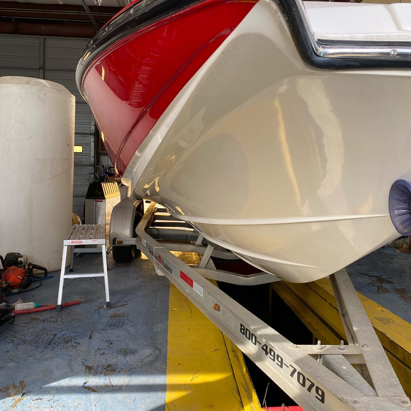 Large white and red boat on a trailer inside a boatyard or garage, with a step stool nearby