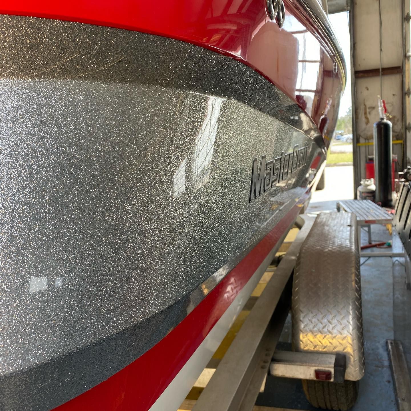 Red and silver boat hull in a workshop, with a metal trailer beside it.