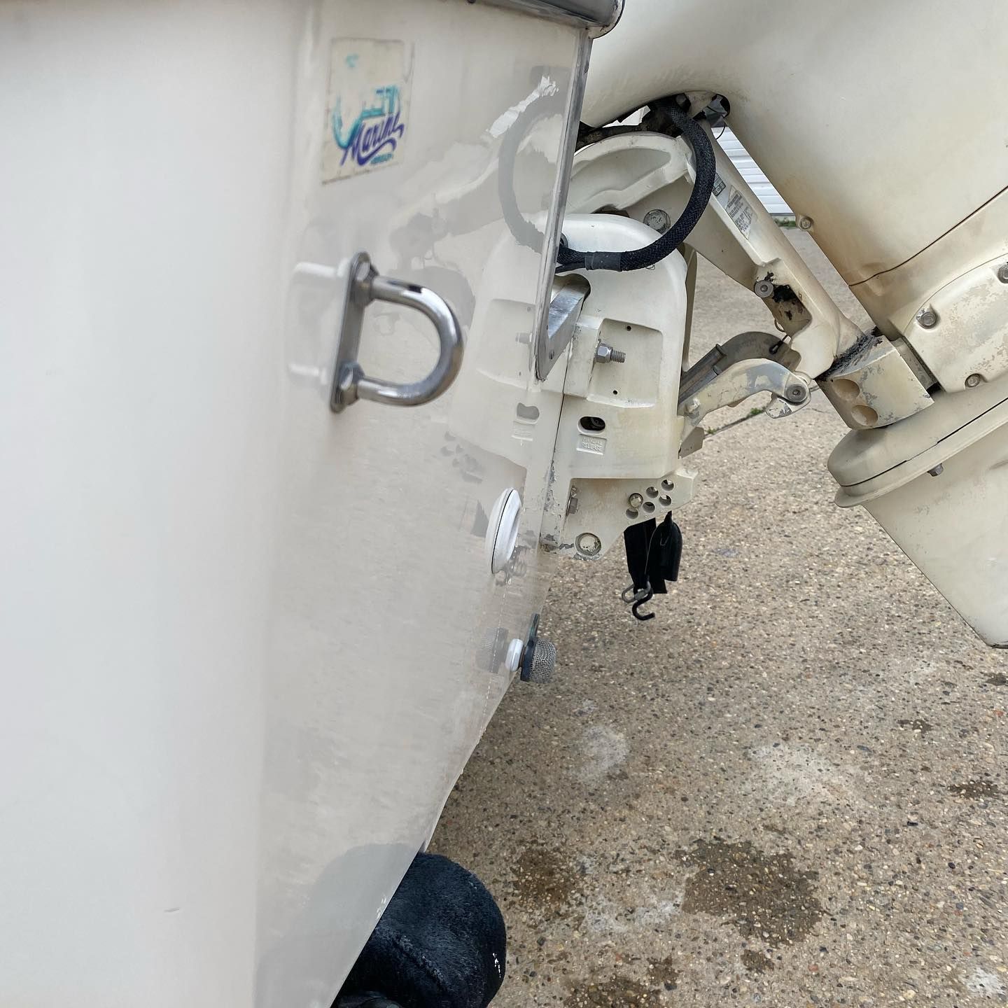 Close-up of a white boat hull with metal fittings and cables on a gravel surface.