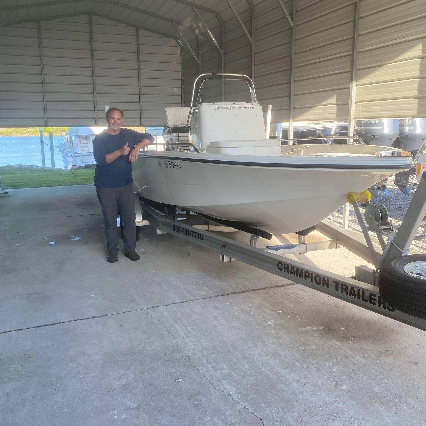 Man standing beside a white boat on a trailer inside a covered storage shed