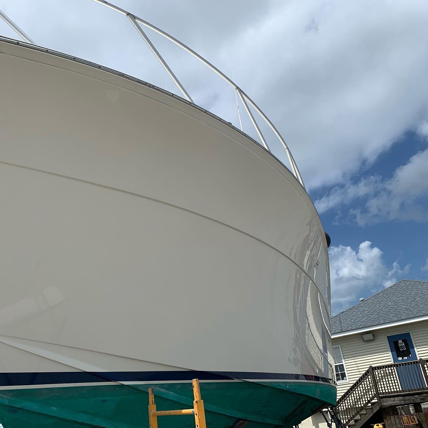 White sail-like structure under a cloudy blue sky, with metal supports and scaffolding below