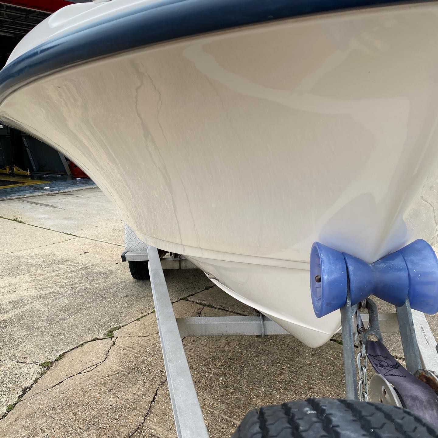 White boat hull on a trailer, close-up of blue bow cover and support straps on pavement