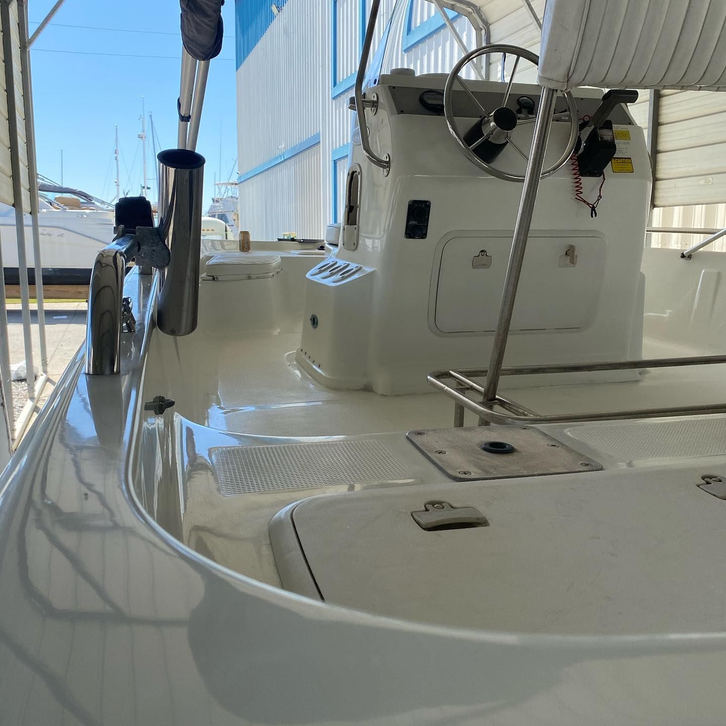 White sailboat cockpit and deck beside blue dock walls, with rails, wheel, and calm water visible.