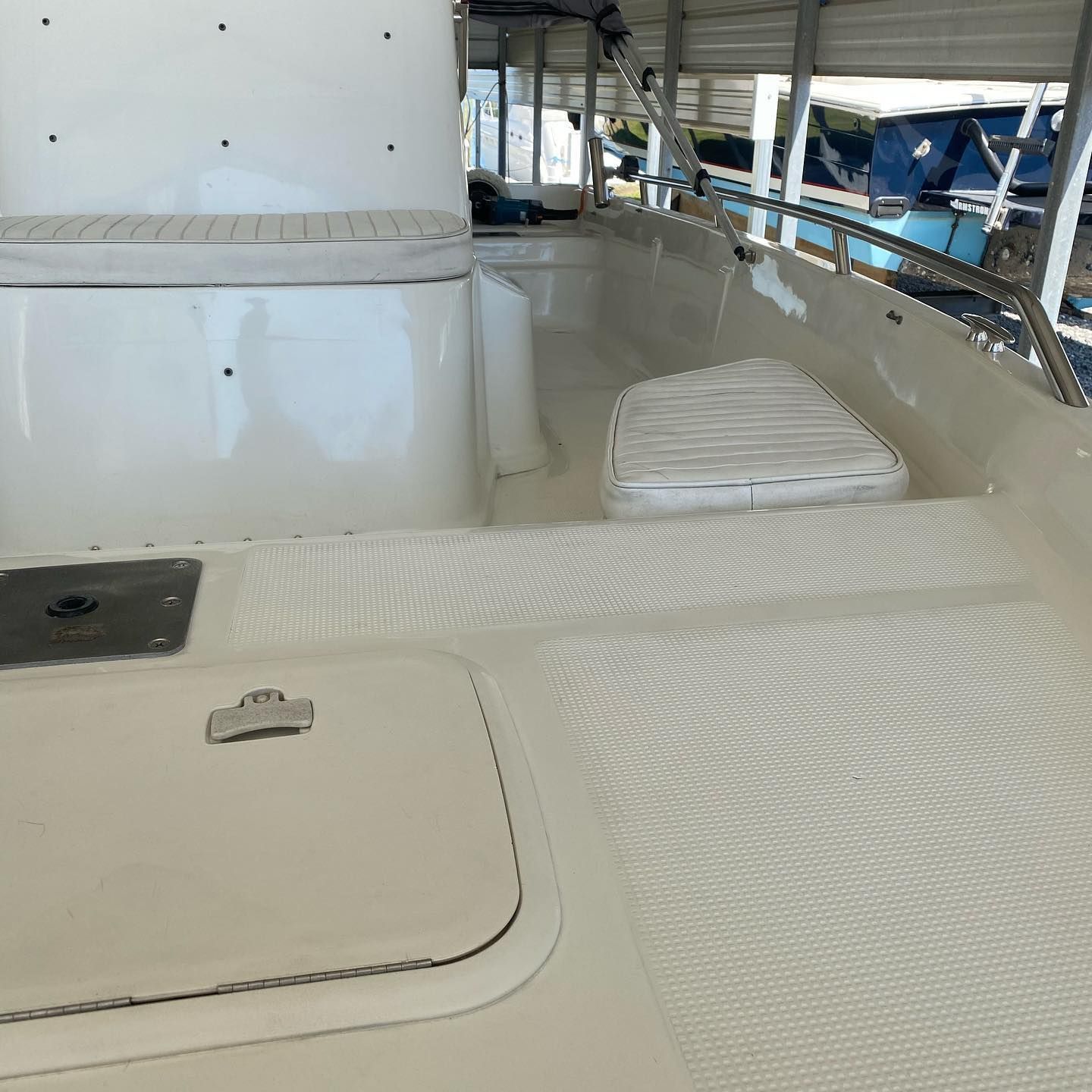 White boat deck with a central helm console, cushioned seating, and canopy supports in a marina.