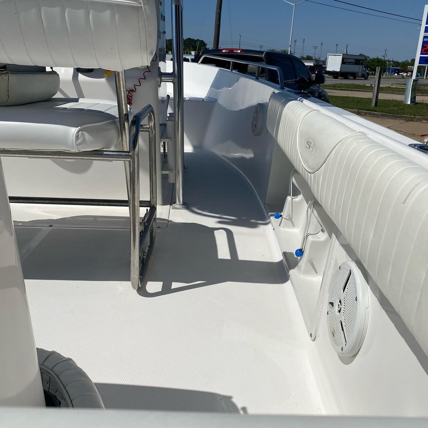 White boat deck with bench seats and speakers in bright sunlight, parked near a road.