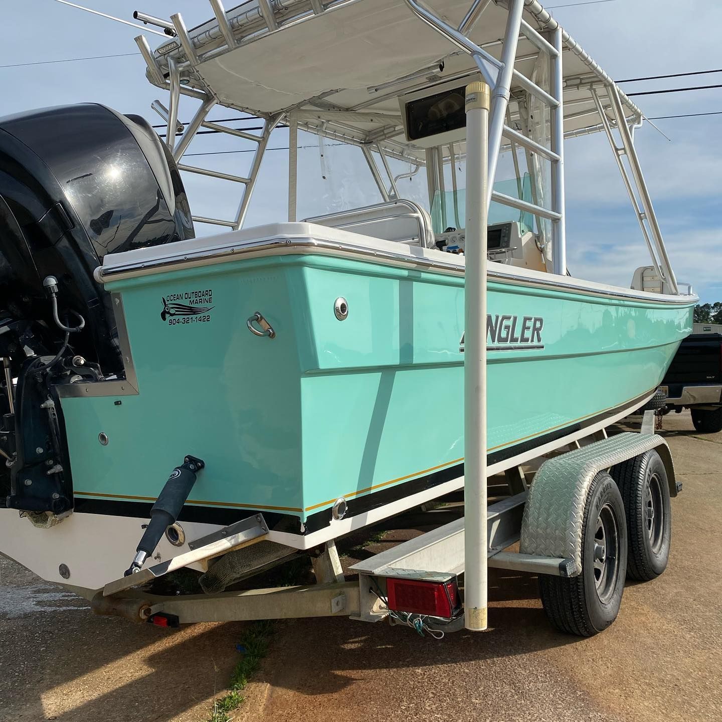 Teal center-console boat on a trailer in a parking lot, with outboard motor and canopy.