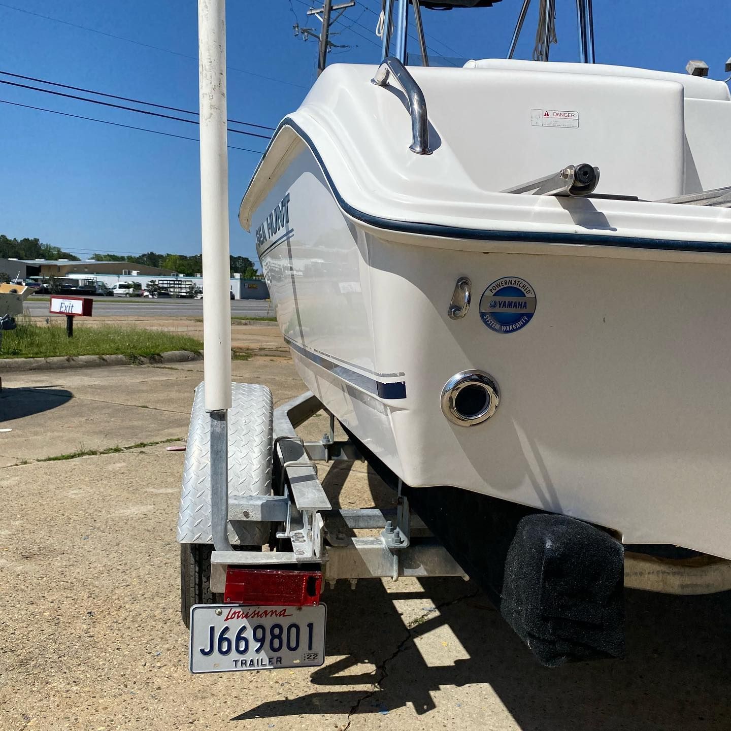 White boat on a trailer with a Florida license plate, parked on gravel in a sunny lot.