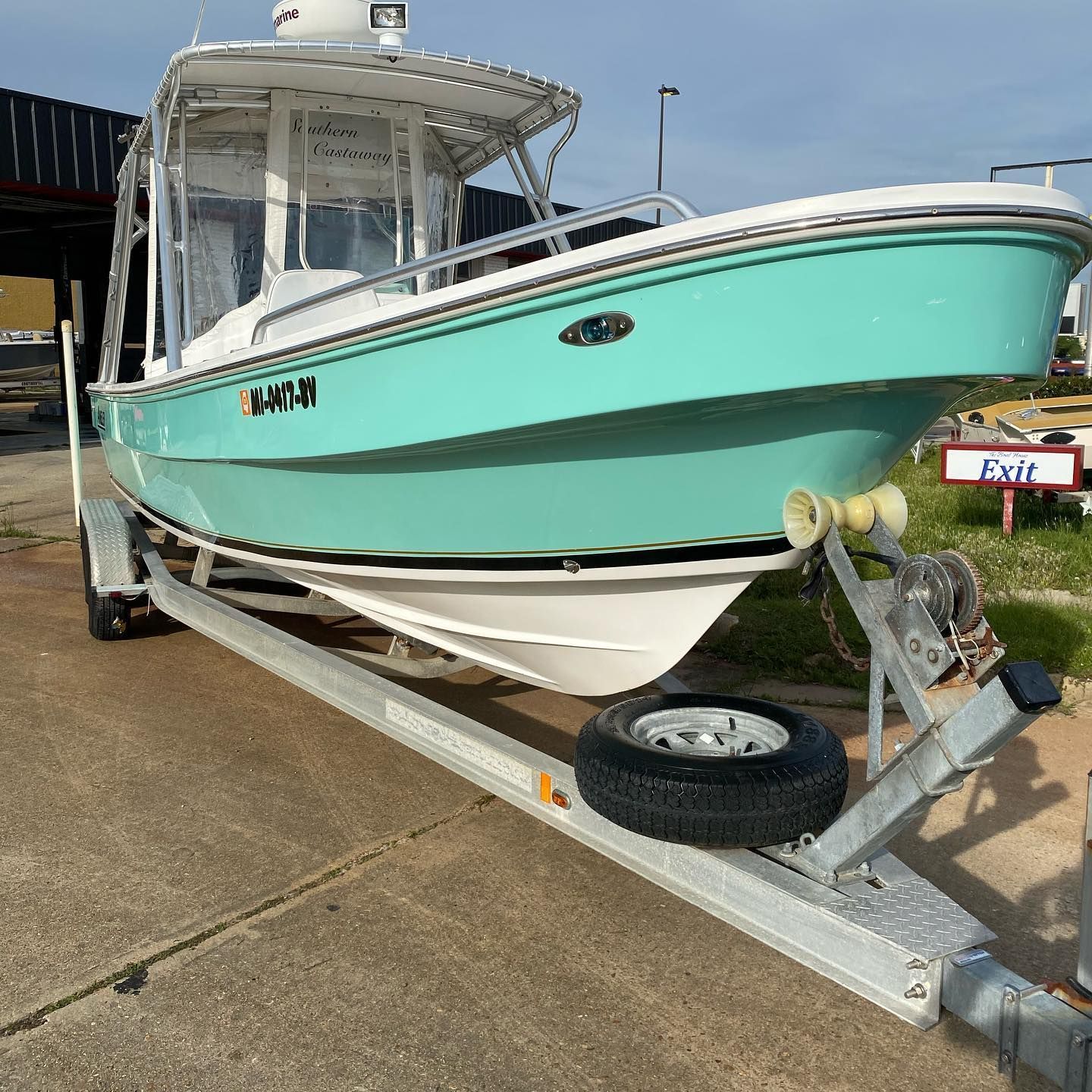 Turquoise center-console boat on a trailer, parked on a concrete lot.