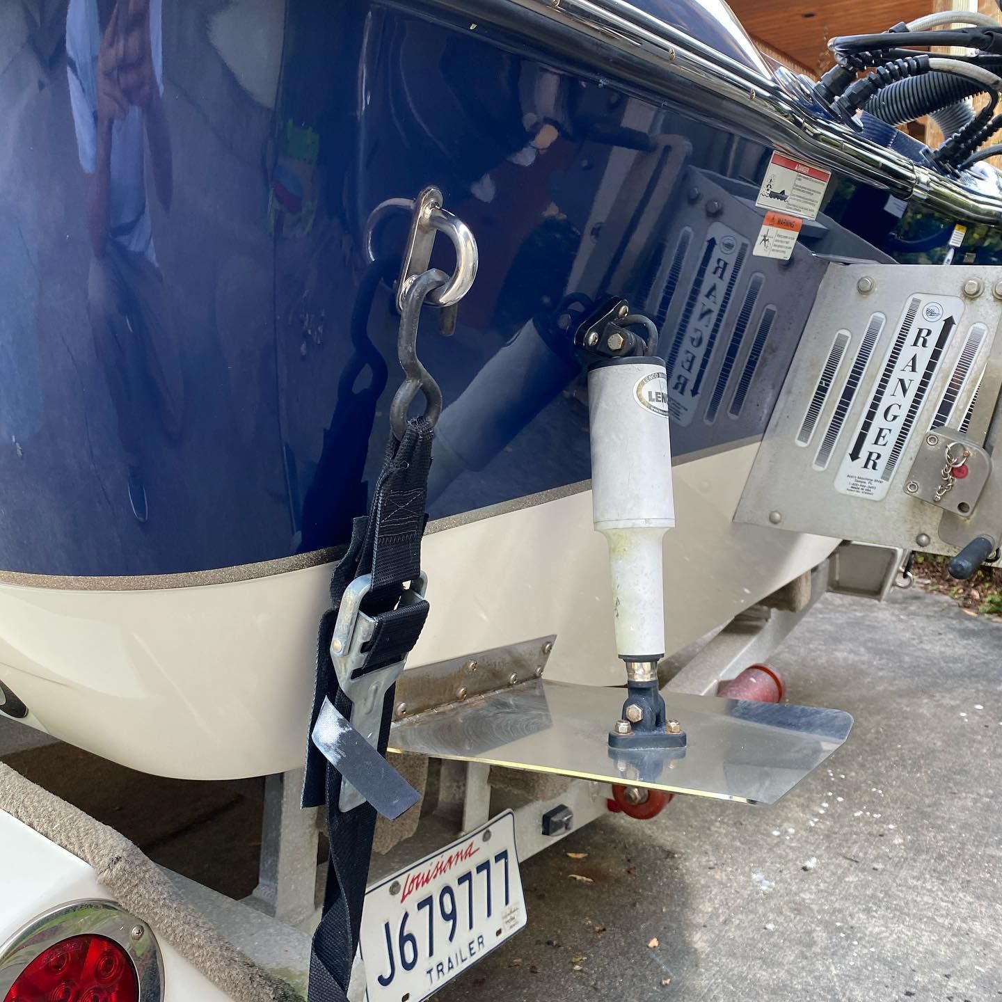 Close-up of a blue-and-white boat stern with hitch, ladder, and trailer license plate.