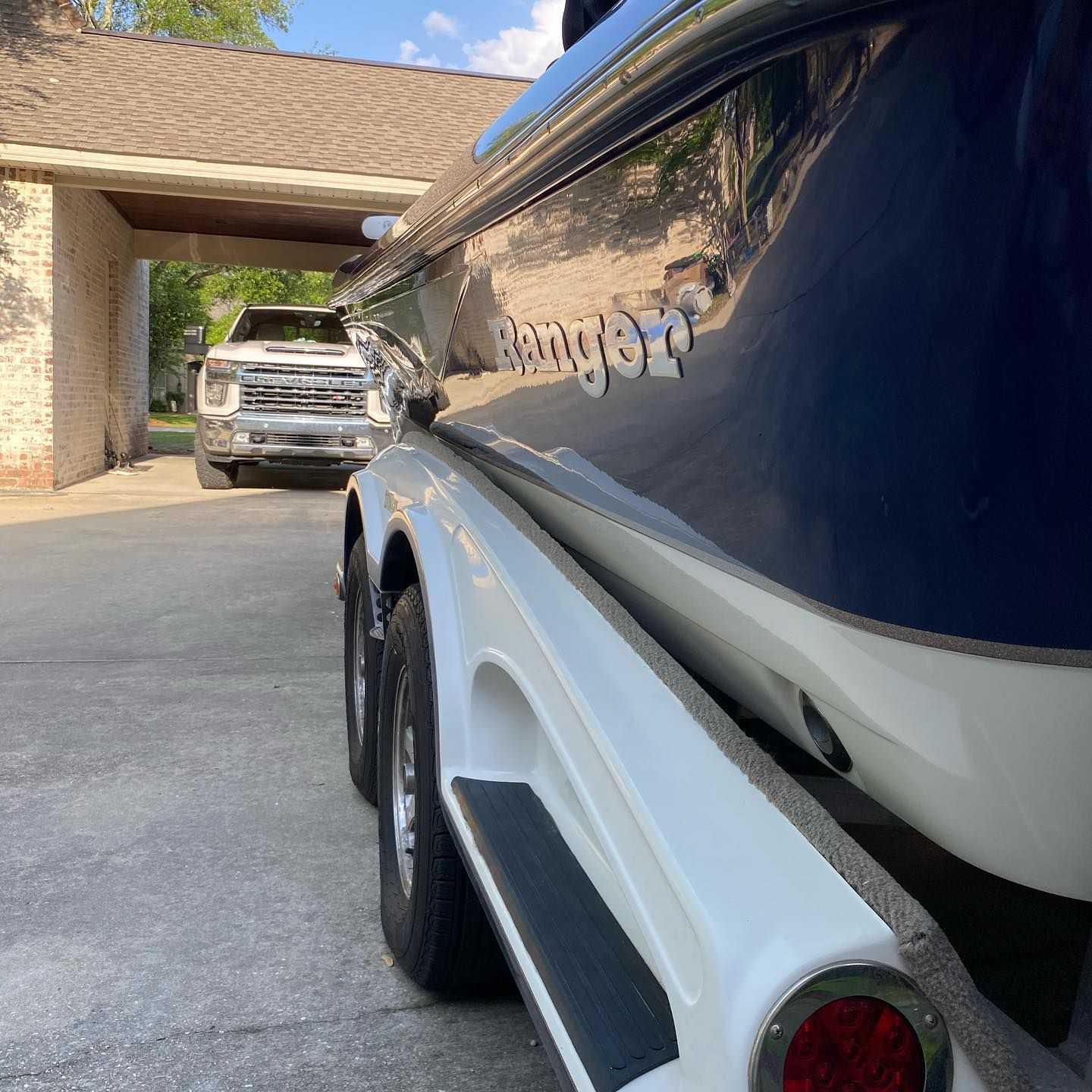 Blue boat on trailer in driveway beside a white SUV under a carport.