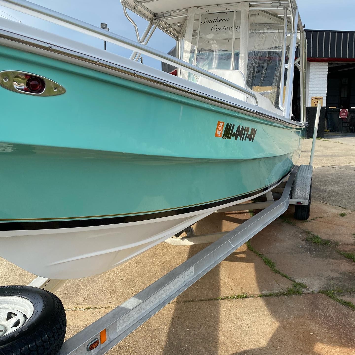 Turquoise and white boat on a trailer in a driveway, with a covered cabin and visible hull details