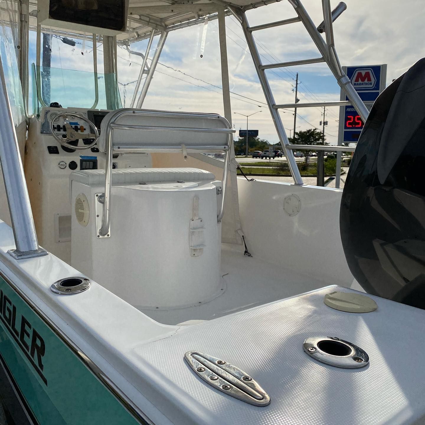 White boat cockpit with helm, seats, and rod holders on the water near a dock