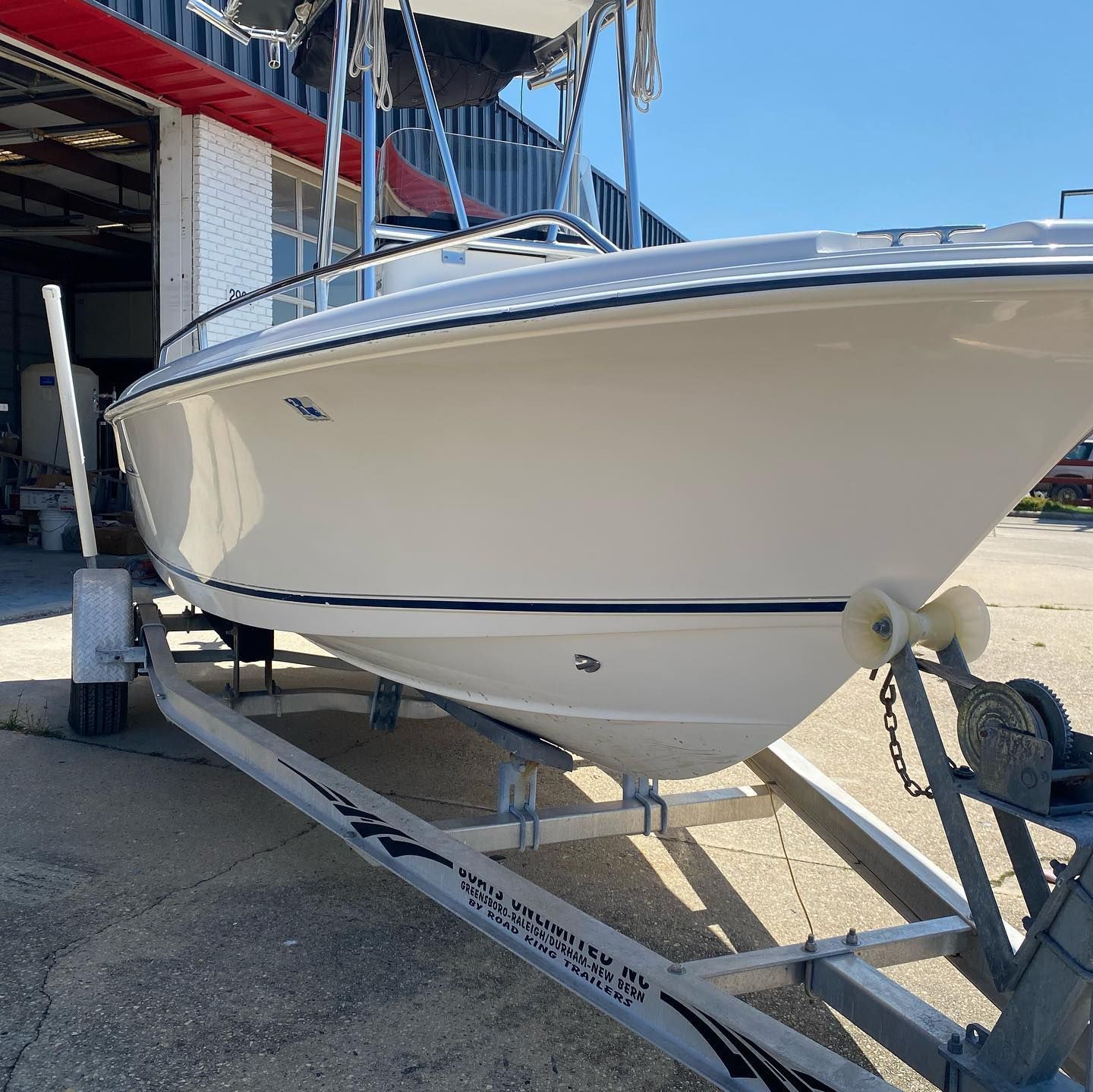 White speedboat on a trailer outside a boatyard under a sunny blue sky