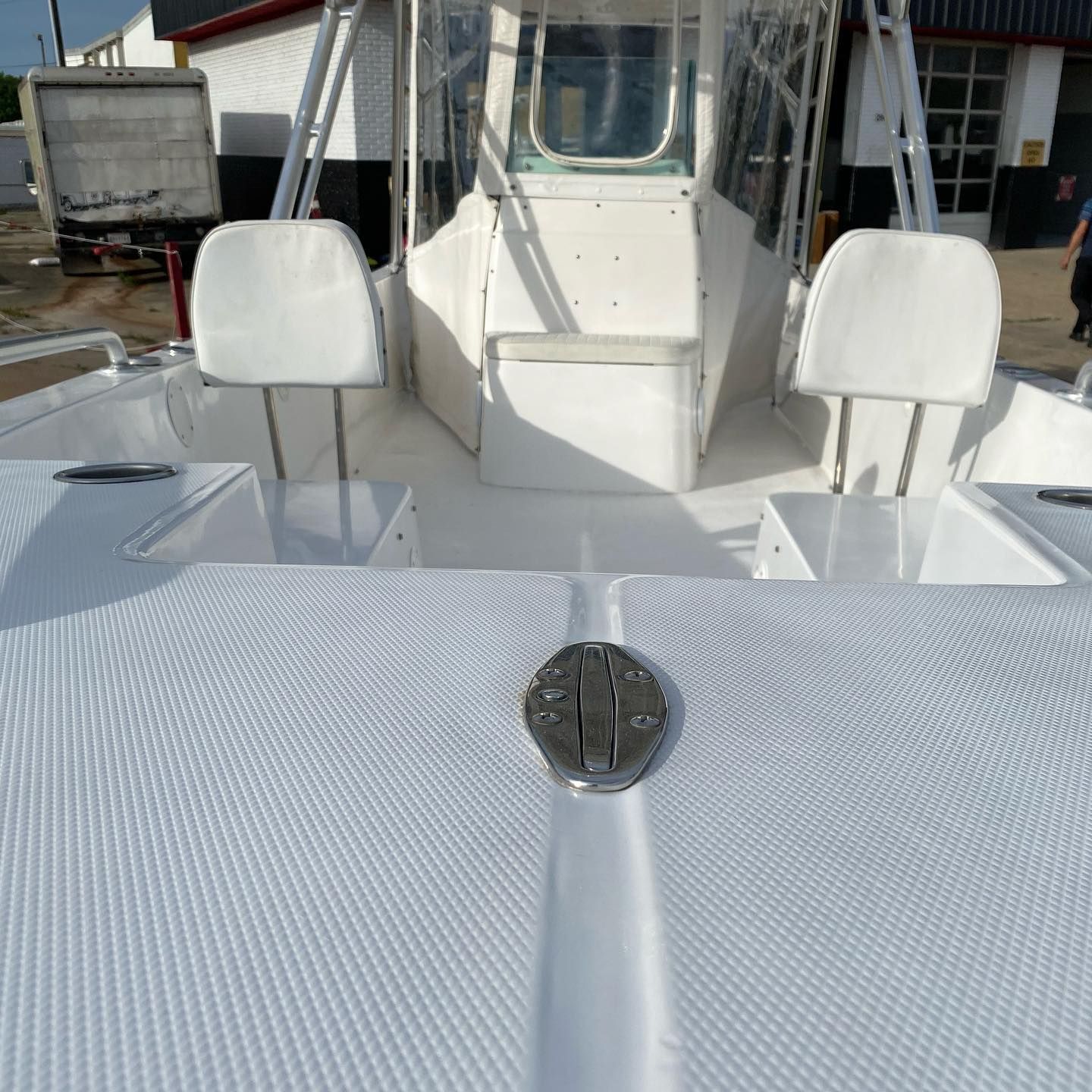 Boat deck with two white seats and a centered hatch on a sunny dockside day