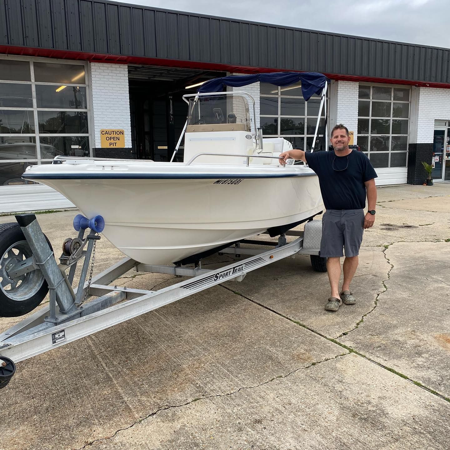 Man standing beside a white boat on a trailer outside a marina building