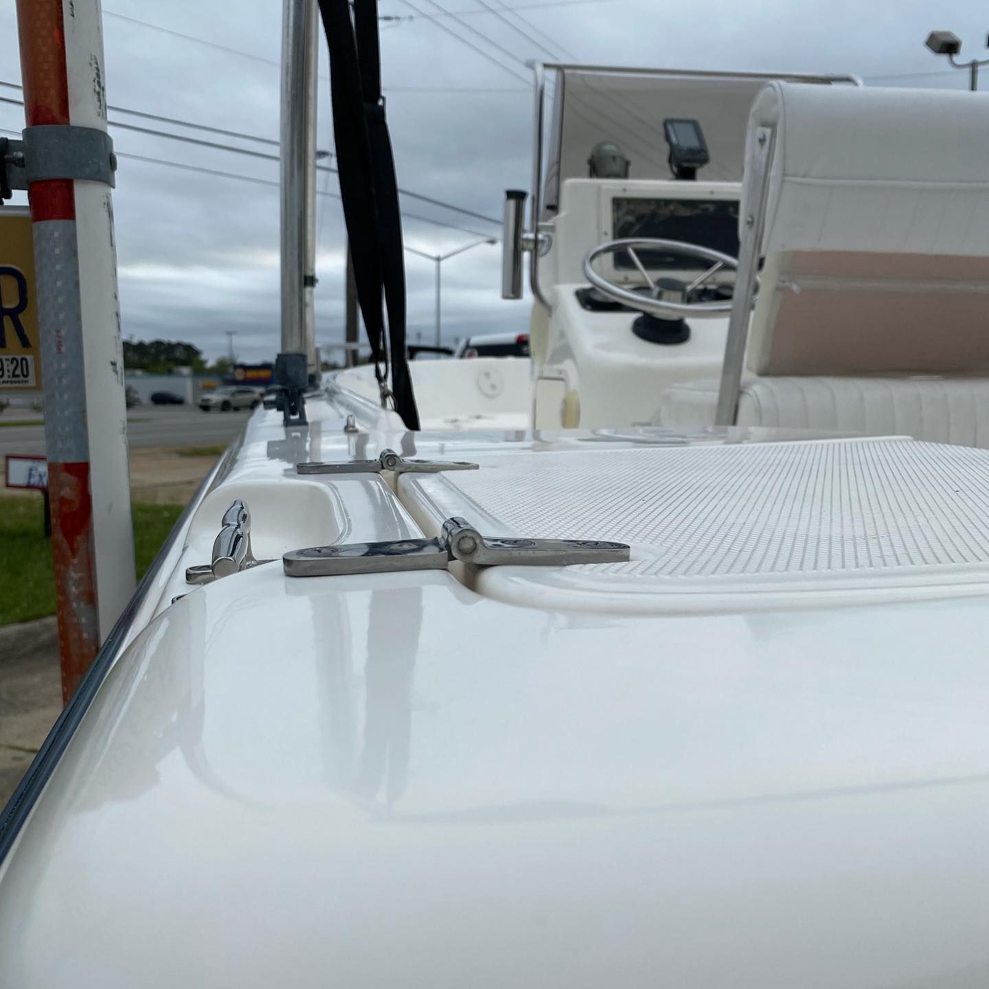 White boat deck with metal rail mounts, docked near a marina under a cloudy sky.