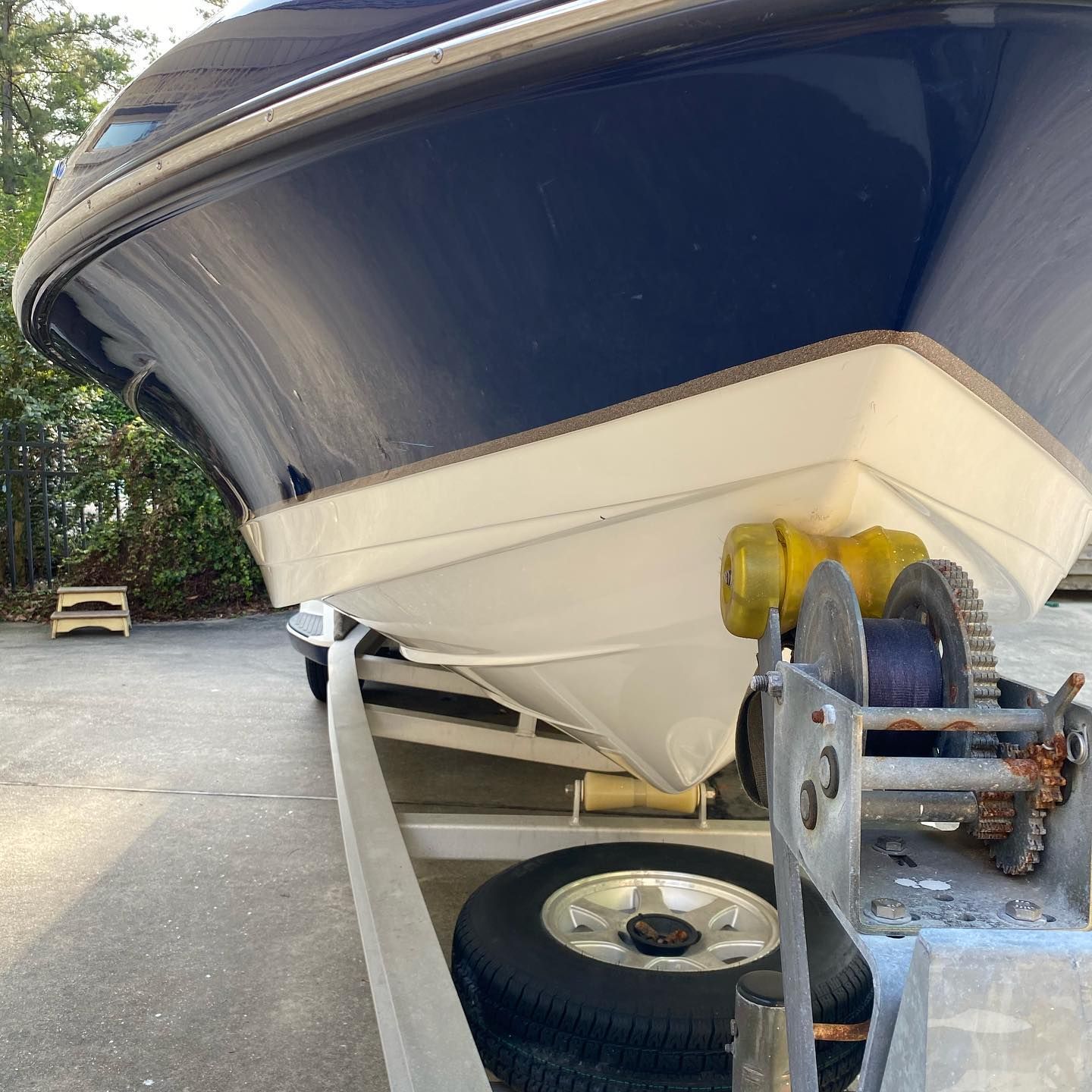 Bow of a blue-and-white boat on a trailer with a winch in a driveway