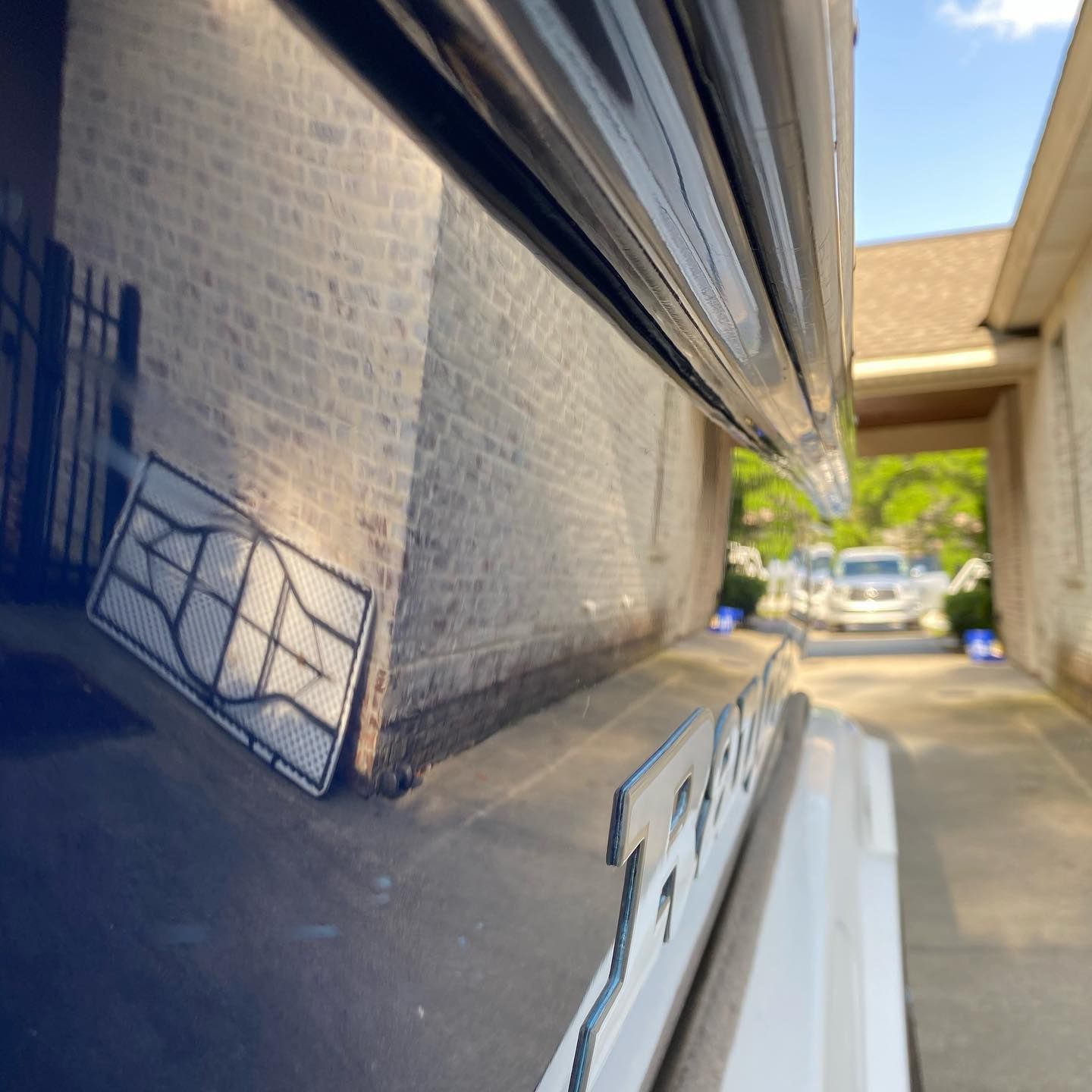Close-up of a glossy black car reflecting a brick wall and gate in a sunny driveway