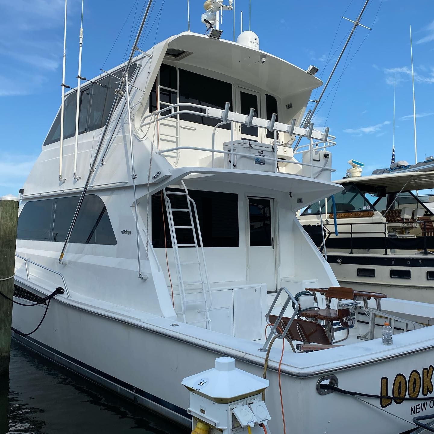 White yacht docked at a marina, with upper and lower decks and calm water beside it.