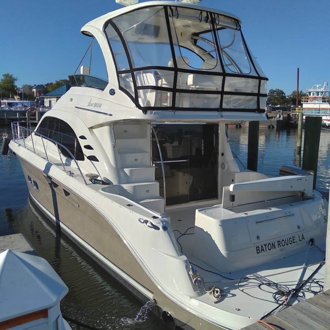 White motor yacht docked in a marina, stern view with beige hull and black canopy under clear blue sky