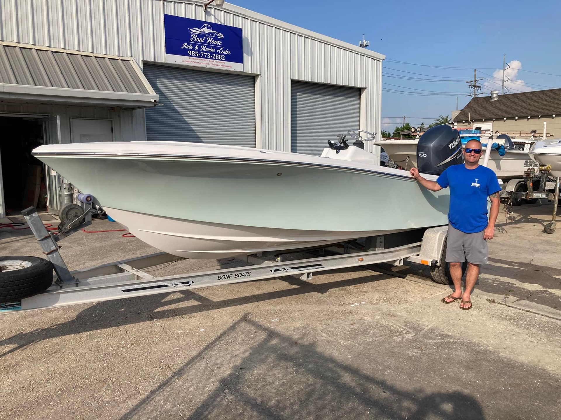 Man standing beside a white boat on a trailer outside a marina building