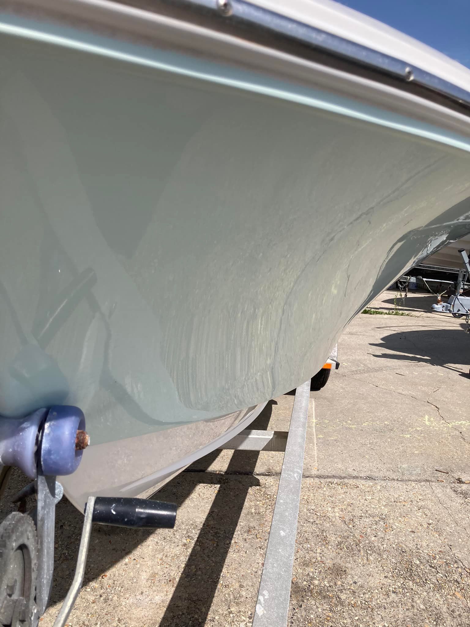 Bow of a pale green boat resting on a trailer in a marina lot.