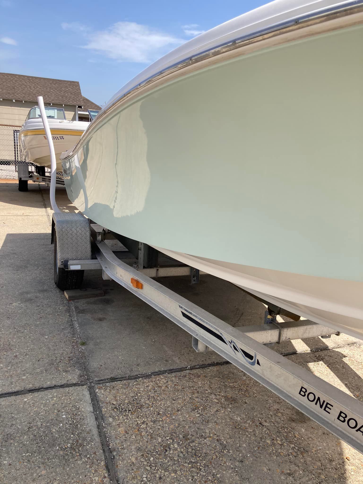 White boat on a trailer in a driveway, viewed from the side on a sunny day.