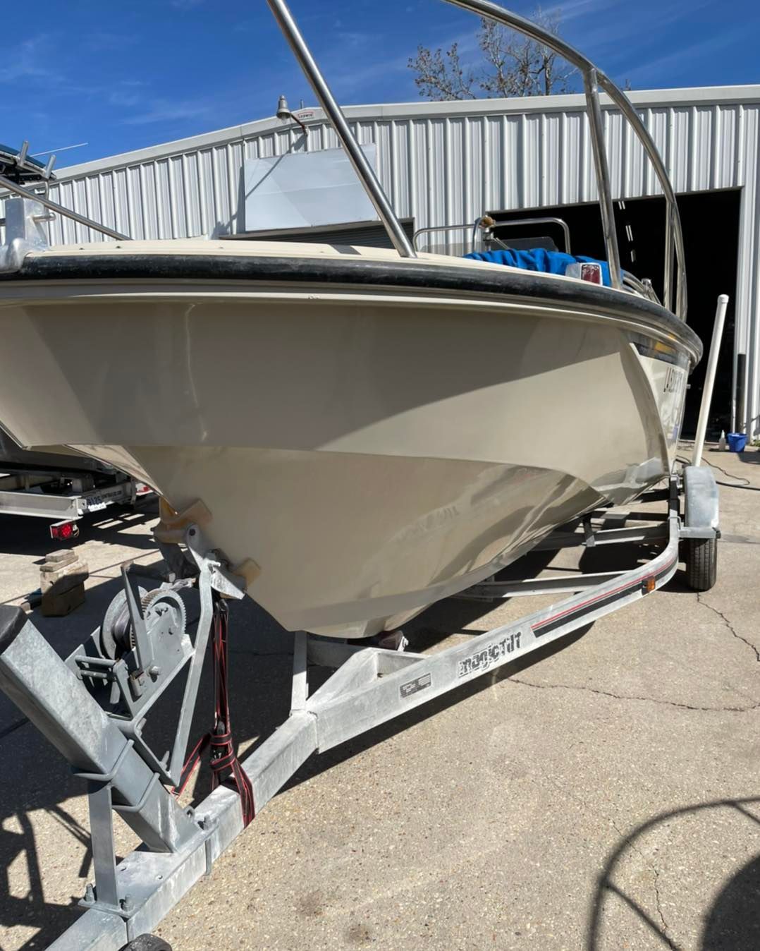 White motorboat on a trailer outside a marina shed, bow facing camera, with metal railings and blue cover.
