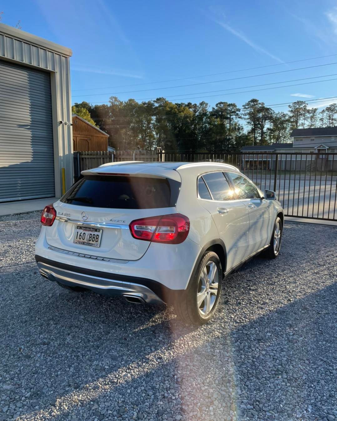White SUV parked on gravel beside a metal shed and fence in bright sunlight