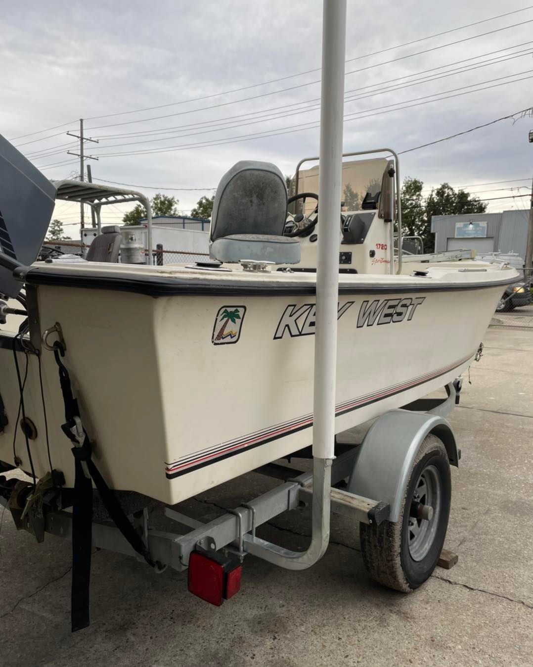 Small white fishing boat on a trailer in a parking lot, with a center console and outboard motor.