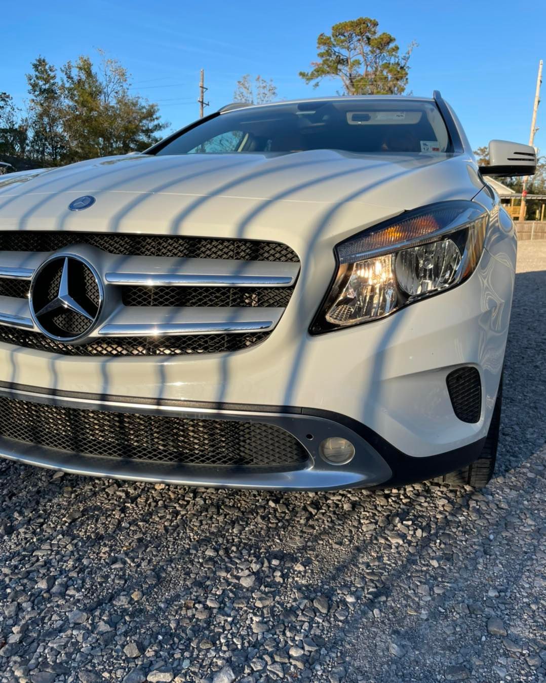 White Mercedes-Benz sedan parked on gravel under a sunny blue sky, front view.