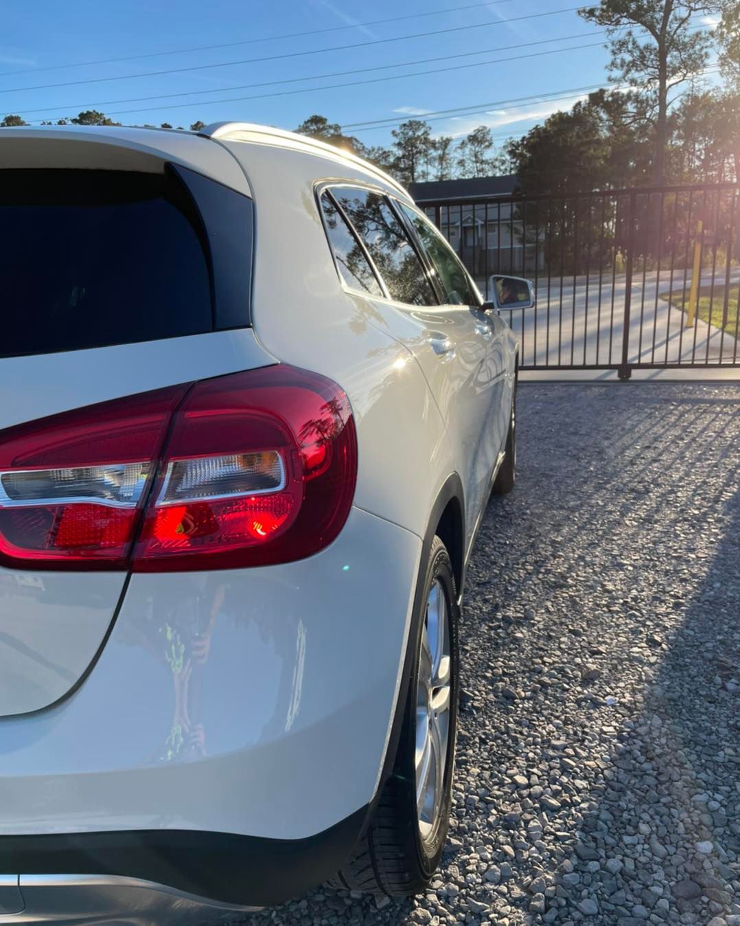 White SUV parked on gravel near a metal gate in bright sunlight.
