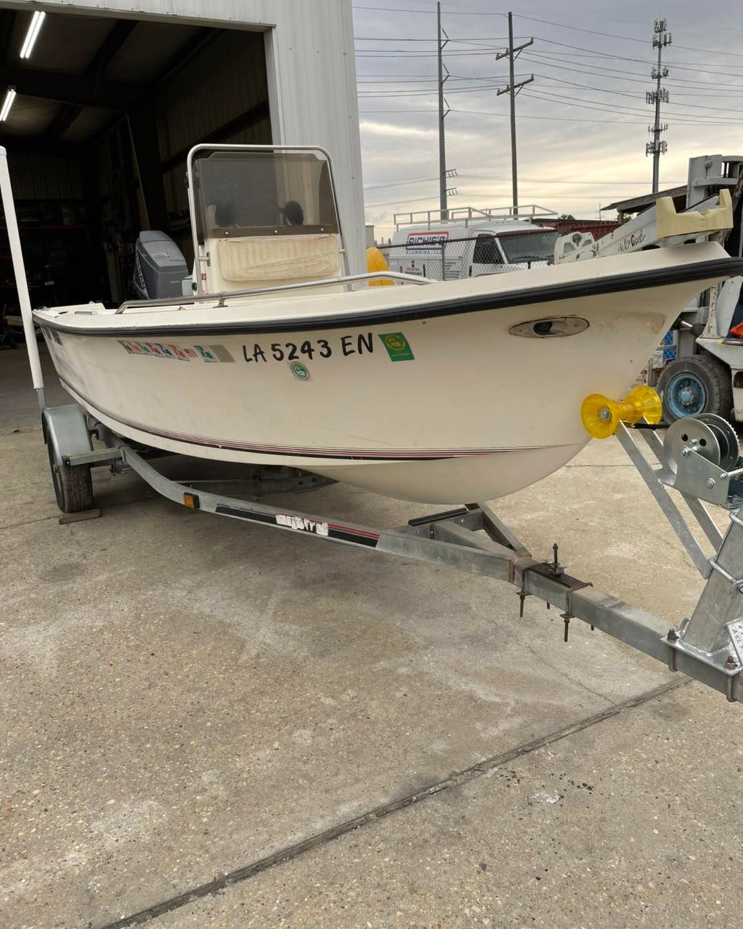 White fishing boat on a trailer in a marina or boatyard, with a windshield and outboard motor attachment