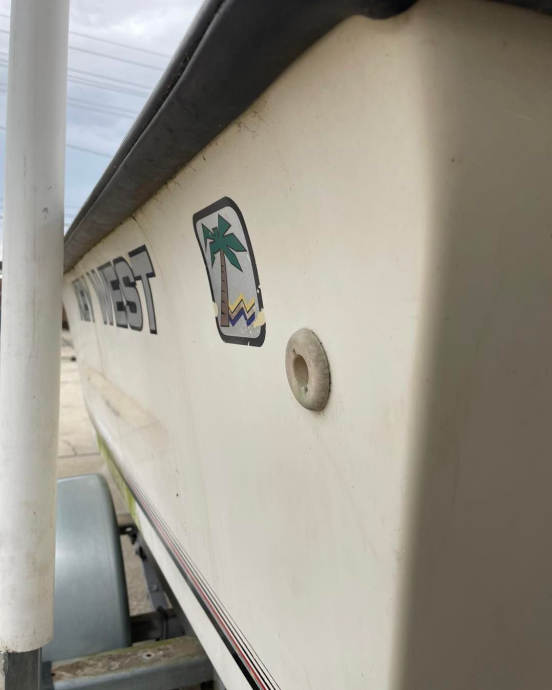 Side view of a white boat hull with small palm tree decals and a round fitting near the edge
