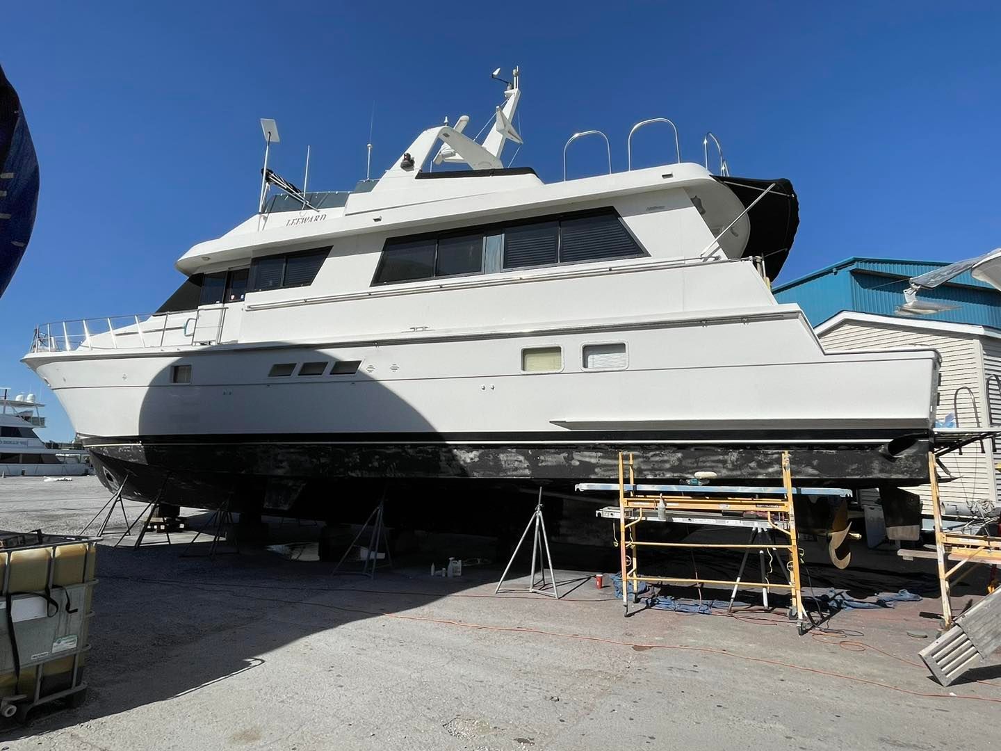 Large white yacht on stands in a boatyard under a clear blue sky