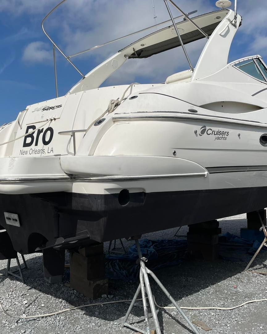 White cabin cruiser boat on stands in a boatyard, viewed from the stern under a bright sky