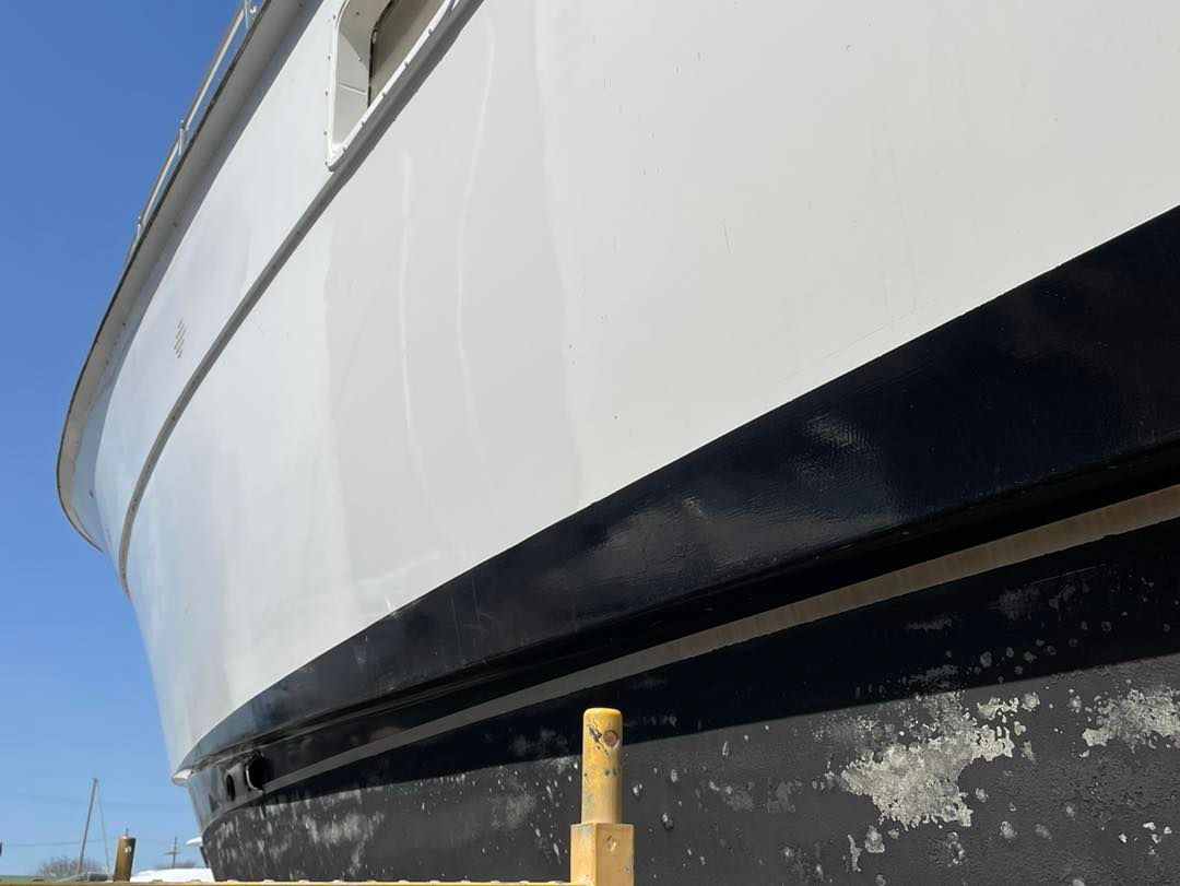 Close-up of a white boat hull above a black lower stripe, with a yellow dock post in front.
