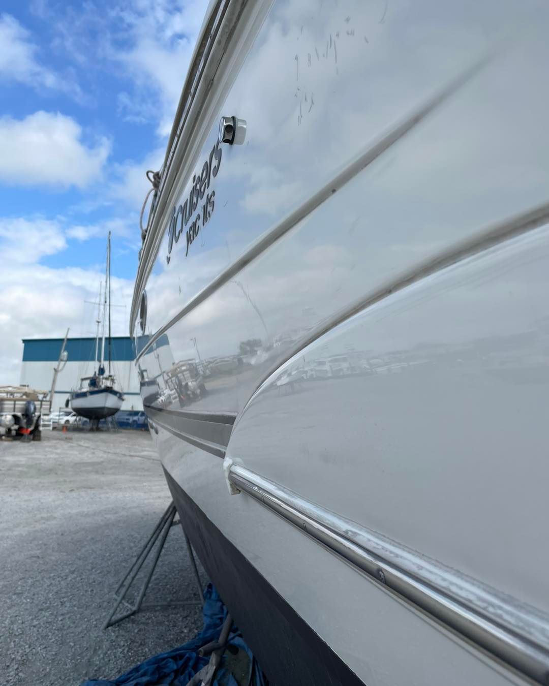 Close-up of a white boat hull on land, with blue ropes and a marina in the background