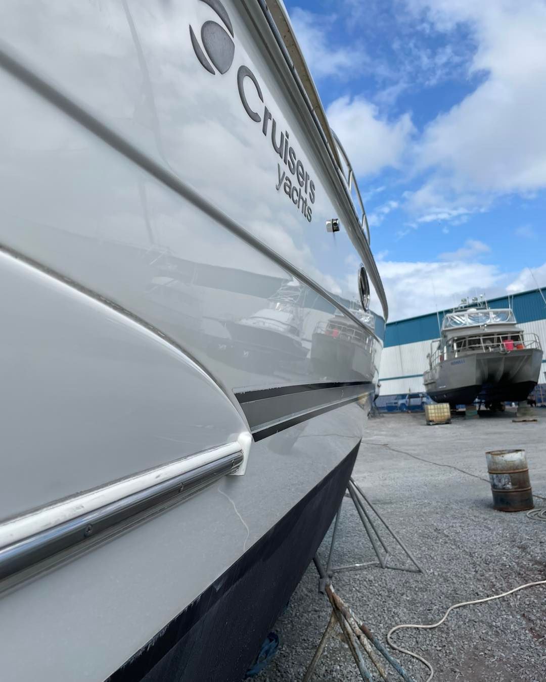 Close-up of a white boat hull at a marina, with another boat and blue sky in the background.