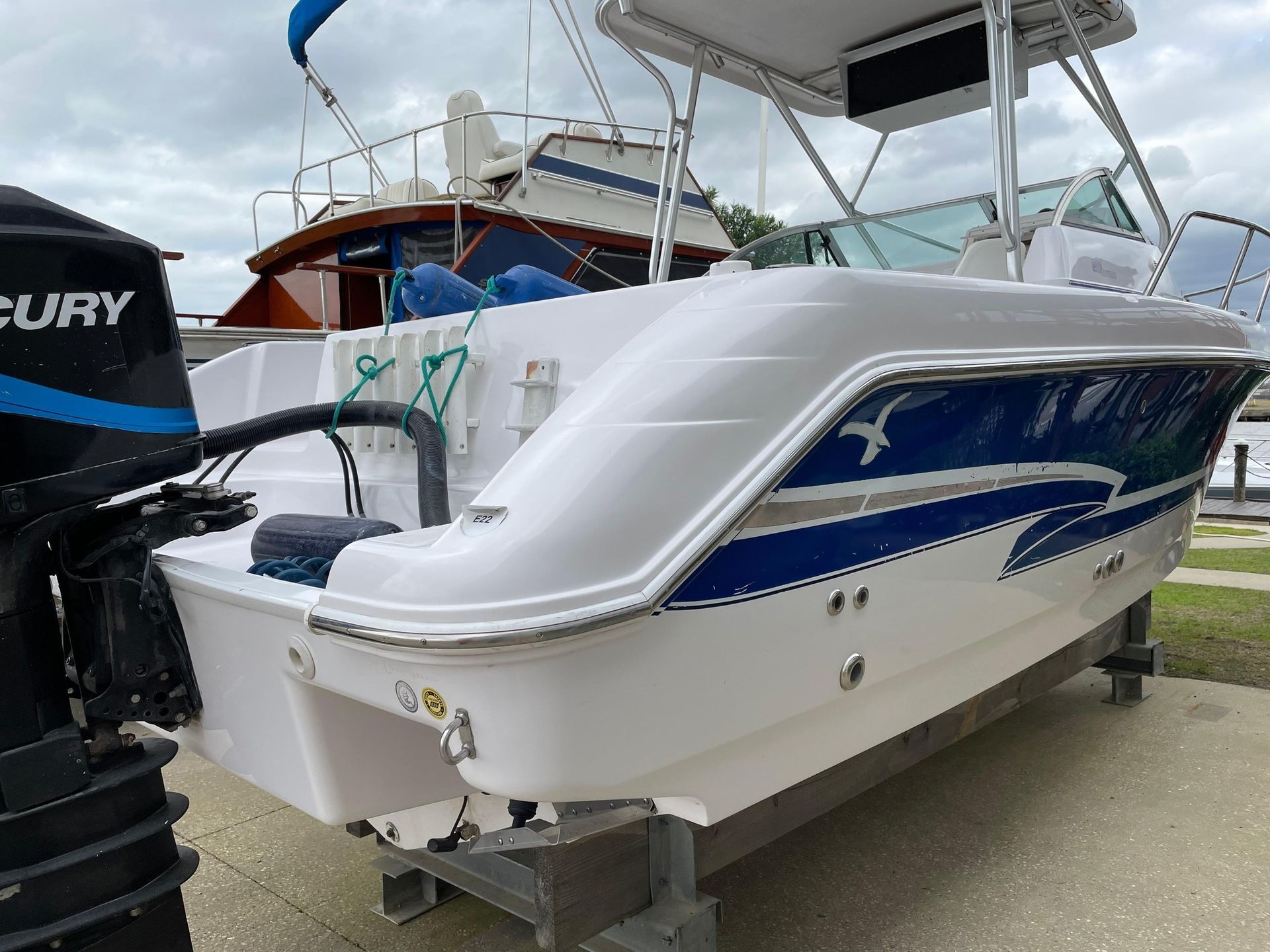 White and blue motorboat on a trailer at a marina, with other boats in the background