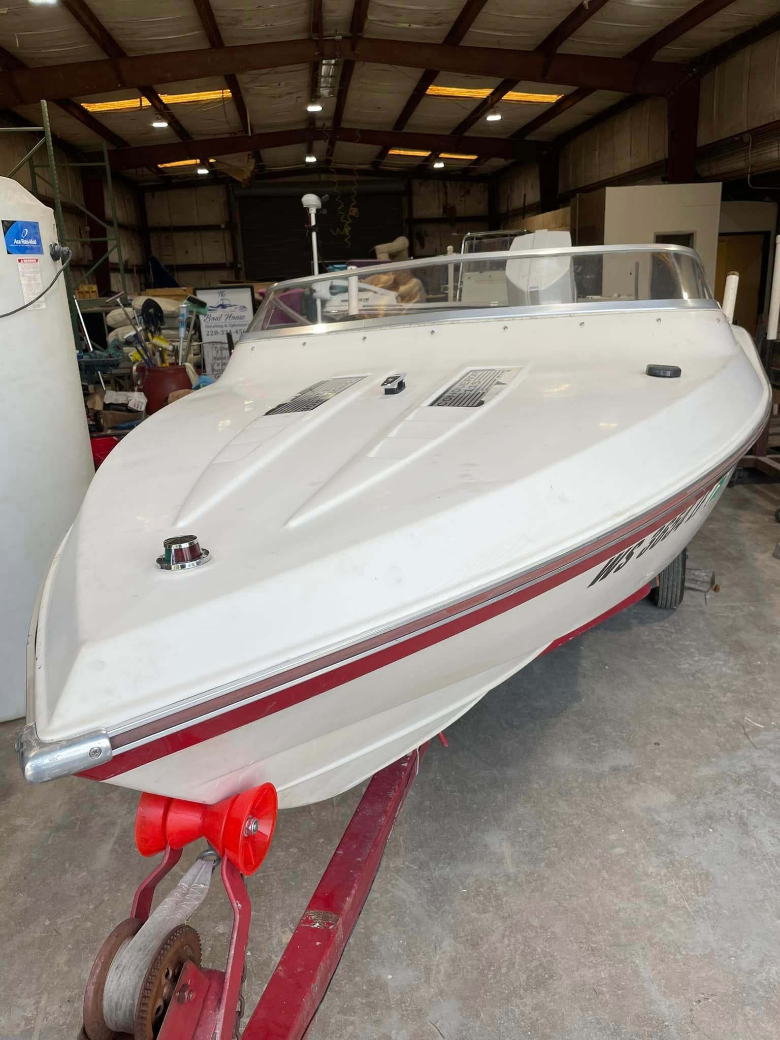 White speedboat on a trailer inside a workshop, with a red stripe and bow cover.