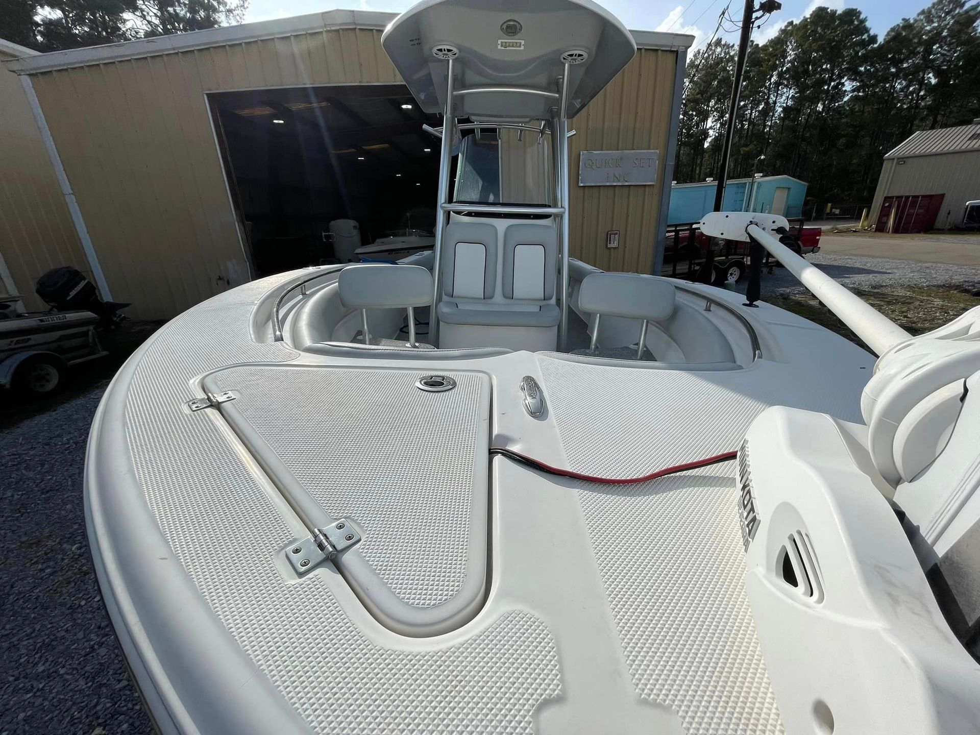 White boat deck with open hatch, railing, and equipment near a dockside building.
