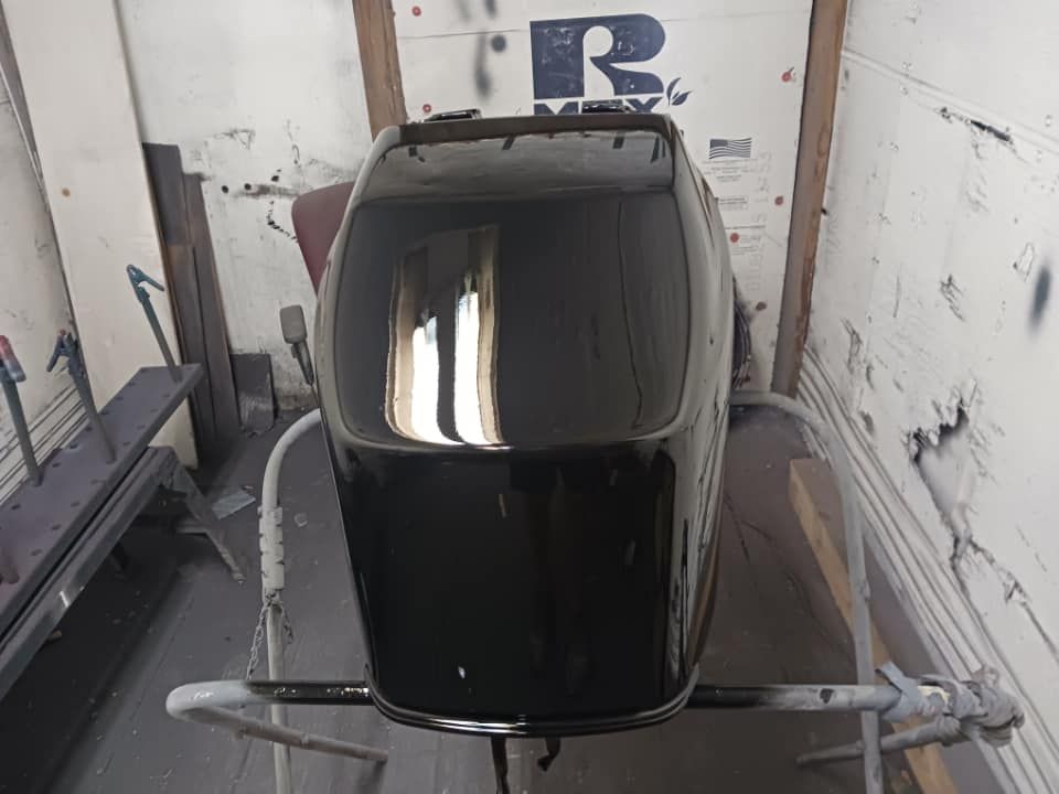 Black car body shell in a narrow paint booth, viewed from above, with reflective roof and side rails