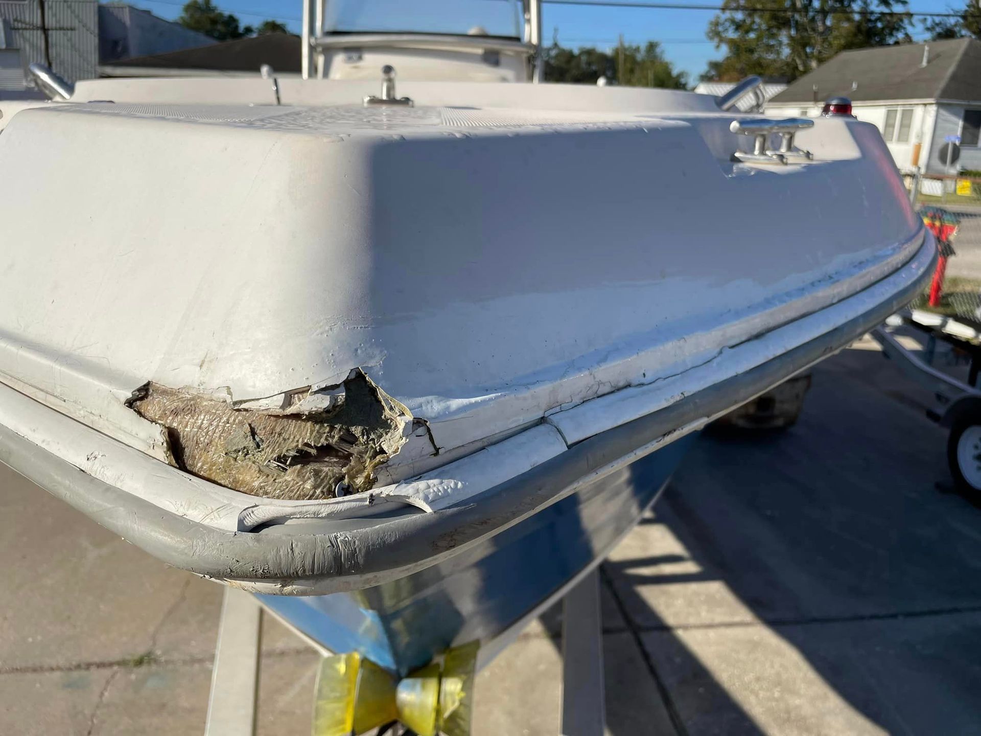 Damaged white boat hull with chipped corner sitting on a trailer outdoors