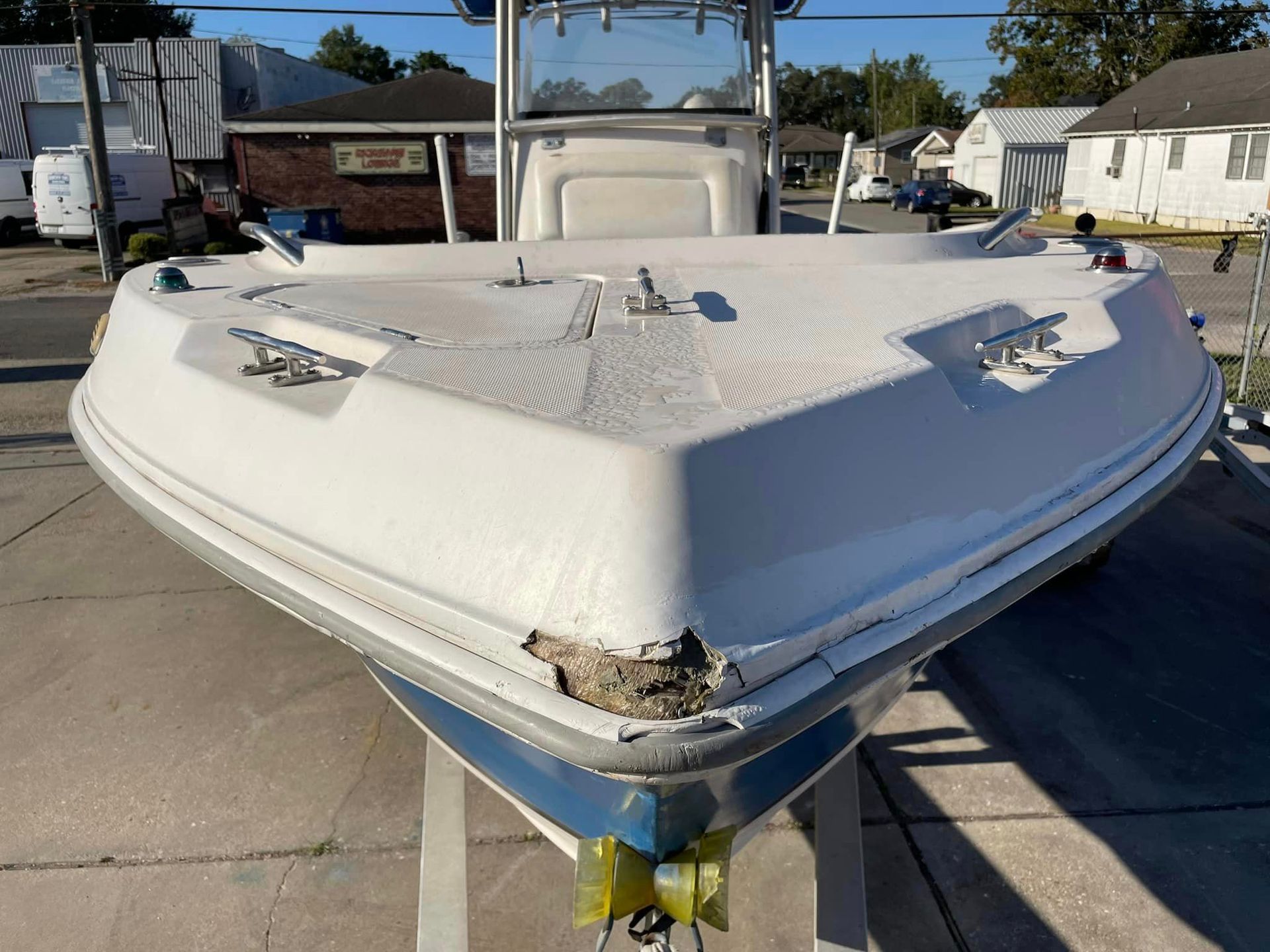 Damaged white boat bow parked on a concrete lot under a clear sky