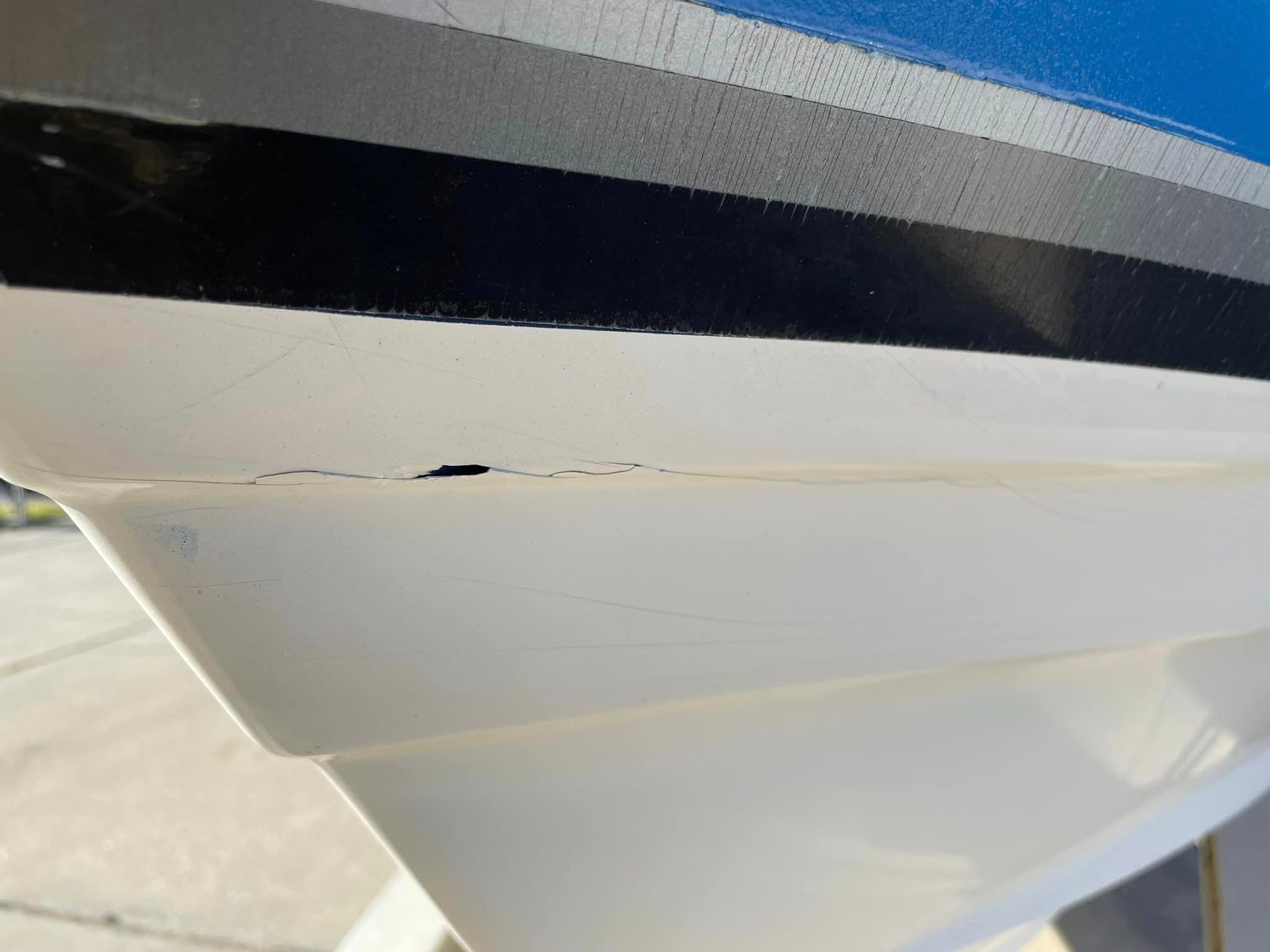Close-up of a white boat hull with a black stripe and visible crack or damage near the waterline