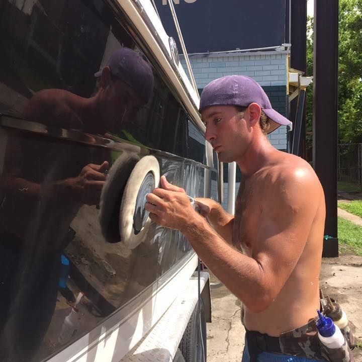 Man polishing a black vehicle with a buffer outdoors in bright sunlight