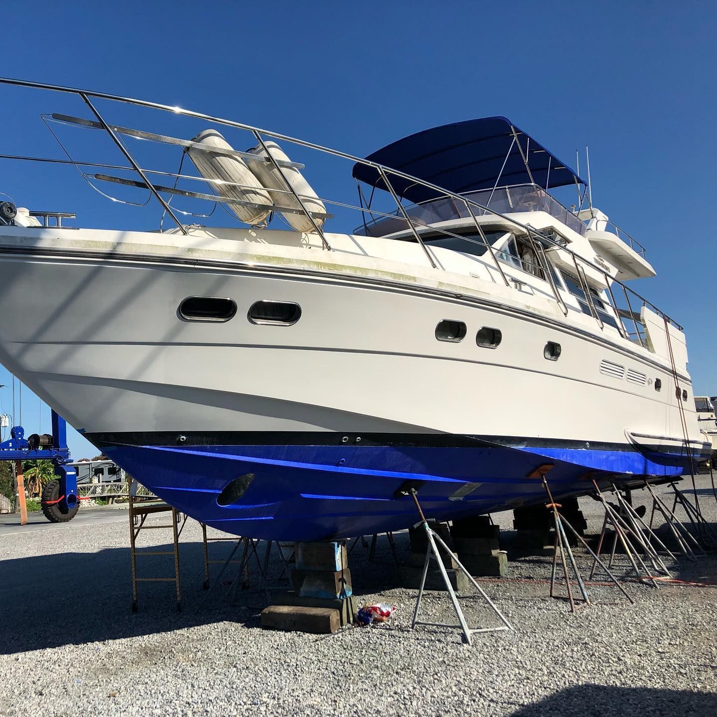 Large white and blue yacht on stands in a boatyard under a clear sky
