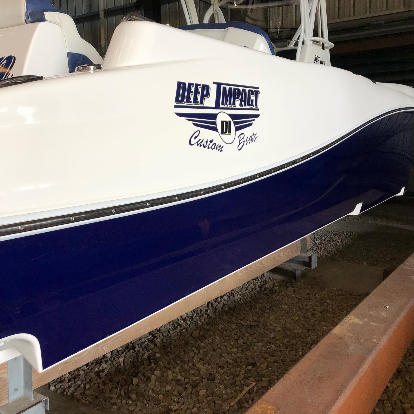 White and navy speedboat on a trailer with Beer Impact logo in a boatyard