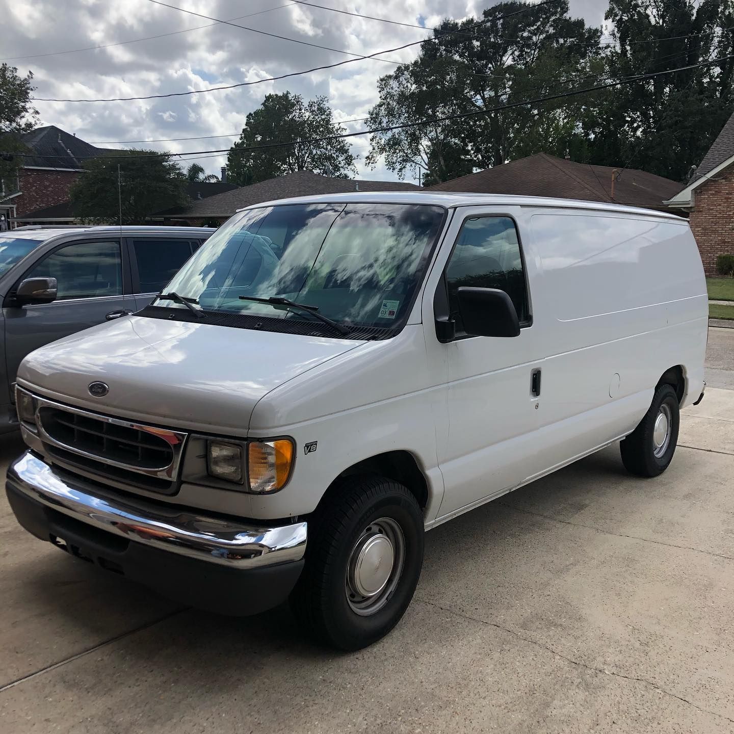 White cargo van parked in a driveway under cloudy sky